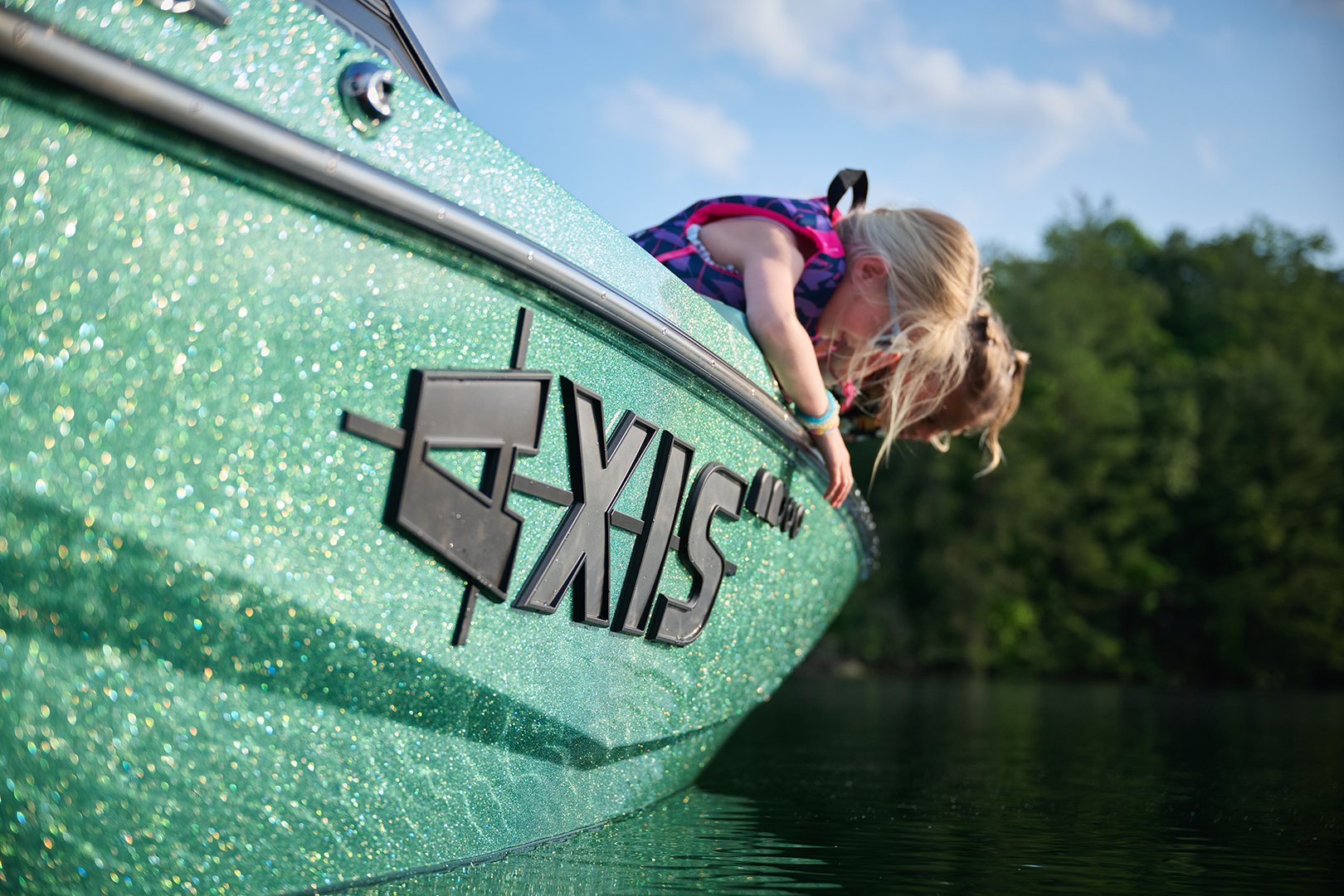 Young girl leans over the glitter-finished Axis A200 bow, smiling at the water.