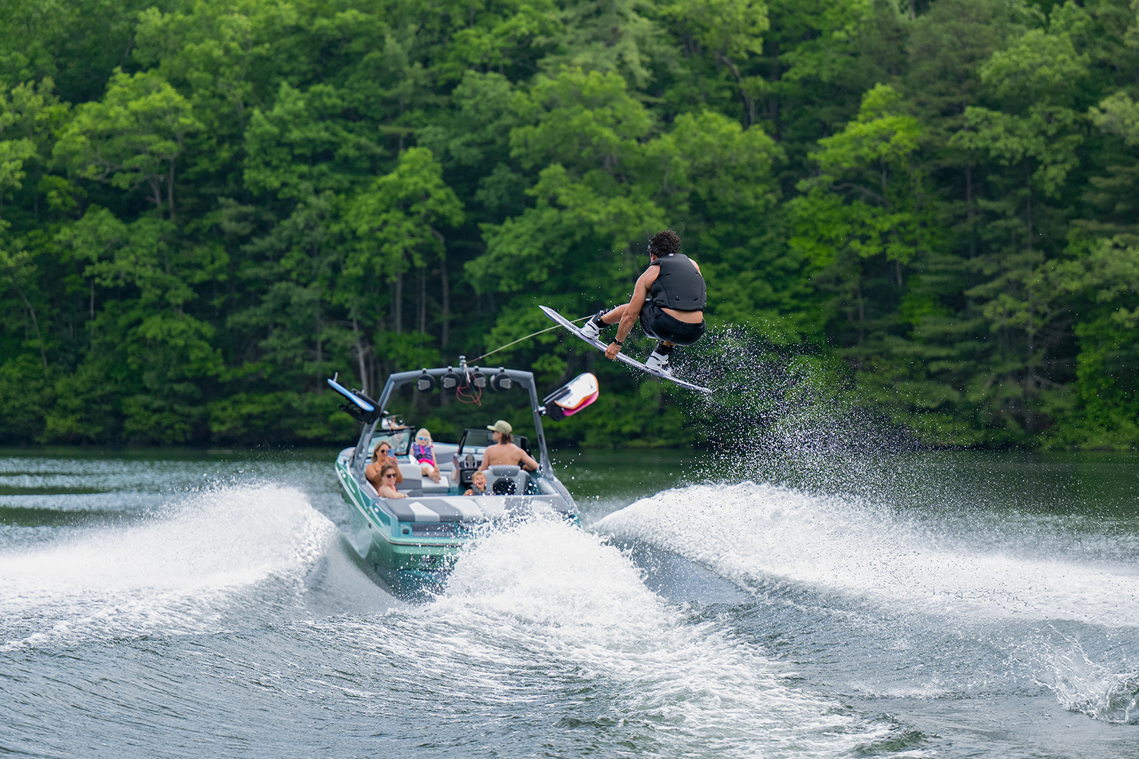 Axis wakeboat powers straight ahead while a rider goes airborne on a wakeboard, showcasing high-performance tracking and speed.