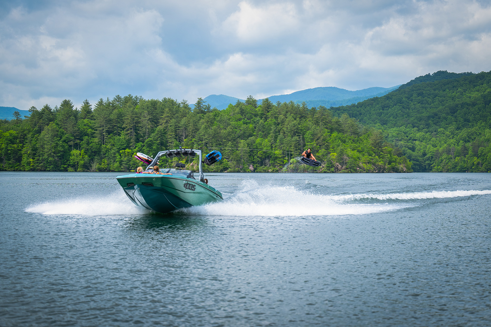 Female wakesurfer rides a clean, surfable wave behind an Axis A225 with multiple passengers on board.