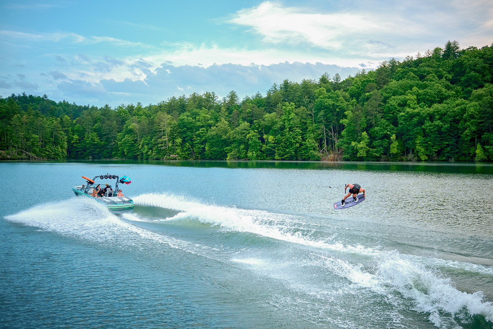 Surfer rides behind a blue Axis wakeboat, demonstrating the control and power of Surf Gate® and Power Wedge® III.