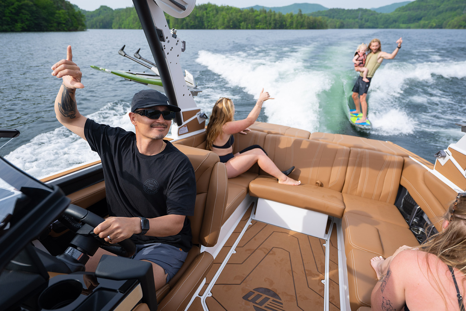 Driver steers Malibu 21 LX while family watches a wakesurfer from rear seating.