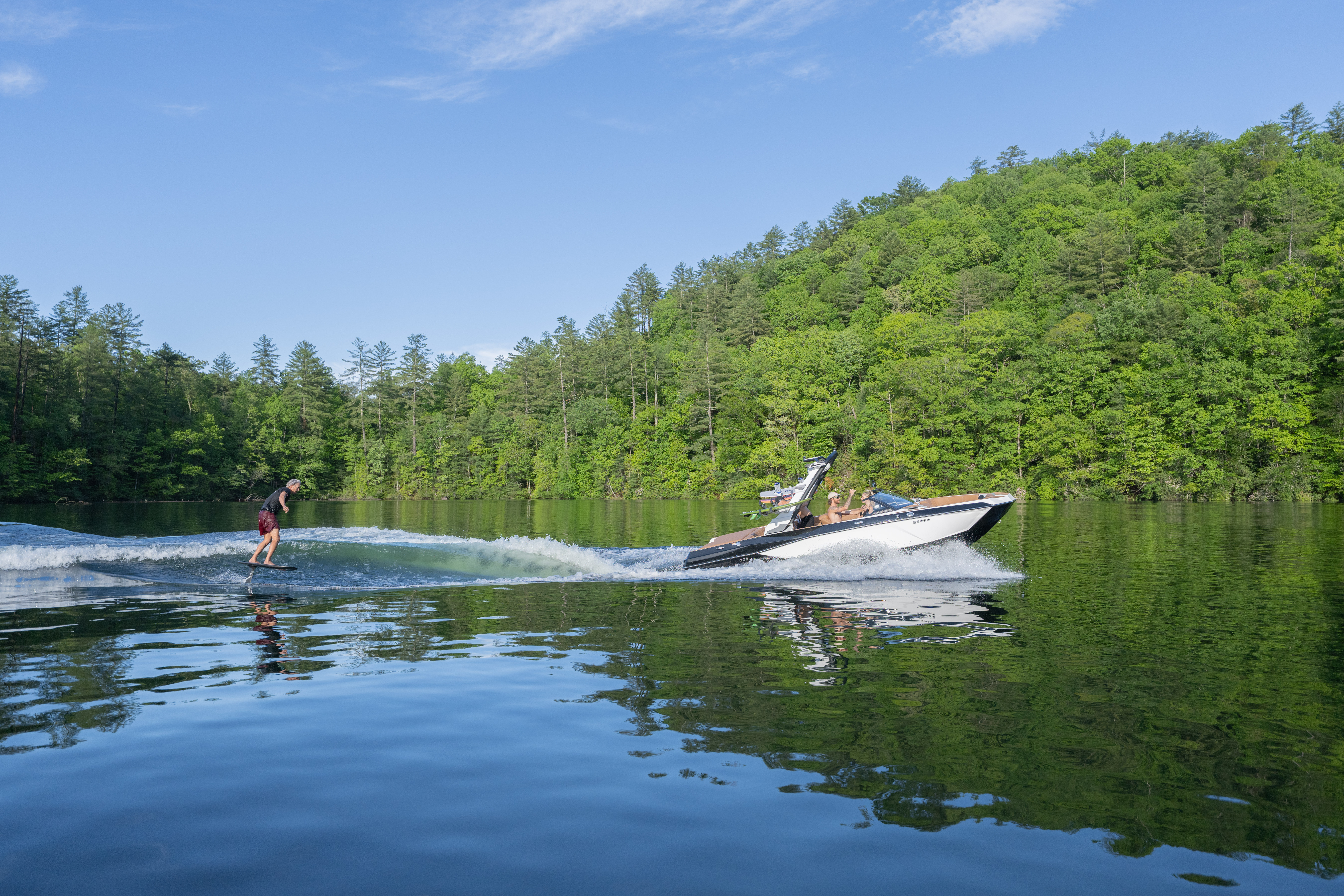 Wakeboarder rides behind a Malibu 21 LX on a glassy, calm lake.