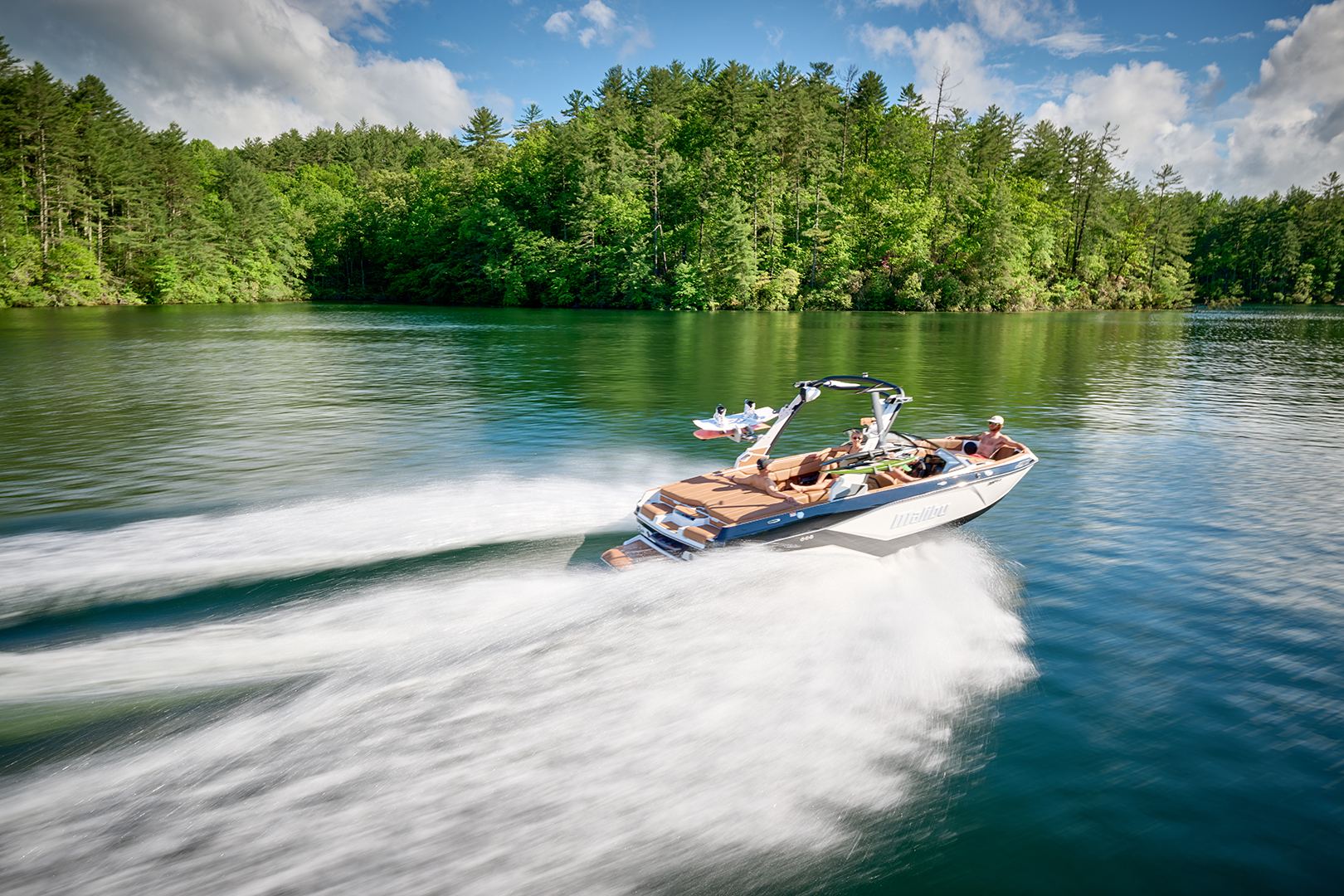 2026 Malibu 21 LX glides across the lake with passengers seated in the bow and lounge, highlighting comfort and spacious layout.